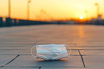Discarded face covering on pavement at sunrise. A symbol of post-pandemic life, caution, and the evolving landscape of public health awareness.