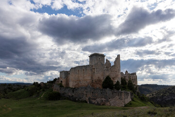 Obraz premium Ruins of rello castle emerging from green hill under cloudy sky