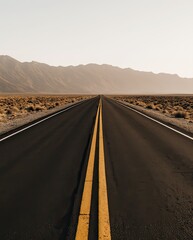 Fototapeta premium Long Yellow Lines on Dark Asphalt Road Leading into Muted Desert Mountains