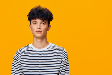 Young man with curly hair wearing a black and white striped shirt stands against a bright orange...
