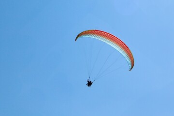 Tandem paragliders soaring through clear blue sky with colorful canopy, enjoying a sunny day adventure and aerial freedom.