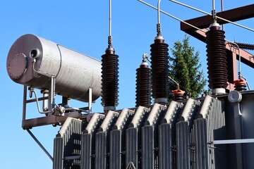 Close-up of a power transformer with cooling fins, high-voltage insulators, and overhead wires....