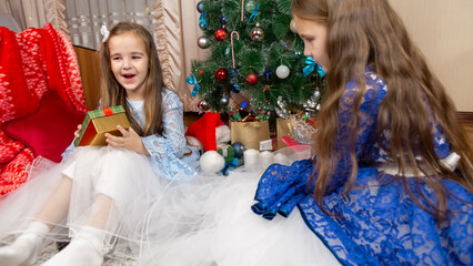 A beautiful little girls in a fluffy festive dress gets surprised with a gift in a Christmas...