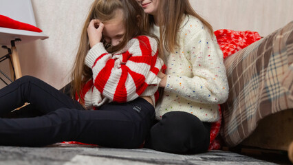 Happy family having fun at home for Christmas. Mother tickles her daughter sitting on the floor. Festive cozy interior