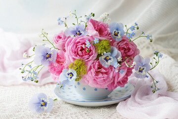 Bouquet of spring and summer flowers in a cup on the table, rose, pansies, forget me not flowers, beautiful postcard, still life, blur.