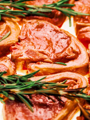 Premium quality marinated lamb loin chops and rosemary herb on white background. Uncooked raw meat on the bone in red color water based marinade to enhance dish taste.