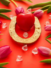 Red heart in golden horse shoe on red color surface and red tulips pointing to the main subject in the center of the image and acrylic gem stones. Meet true love is lucky event concept.