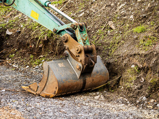 Excavator bucket on the ground. Stone pebble on the ground, soil in the background. Park or house...