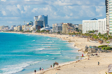 Busy tropical beach in Cancun Hotel Zone with turquoise waves, white sand, and modern resorts lining the coast under a bright sky High-quality photo