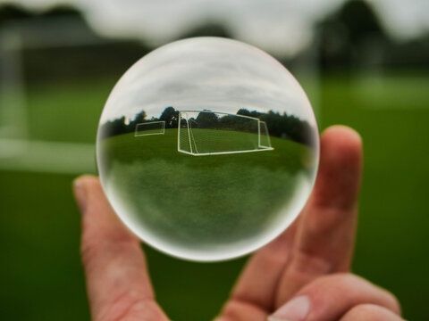 Football or soccer goal posts in glass ball which is hold by a someone hand. Forecasting sport results in popular world sport. Betting on club and national teams concept. Selective focus.