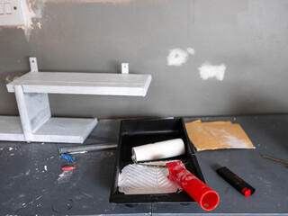 A messy work area with a tray of paint and a roller. The tray is full of paint and the roller is...