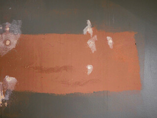 Grey wall during reconstruction work with patch of brown color and white holes left by nails...