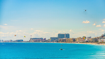Colorful scene of Cancun Hotel Zone with parasailers, boats, and crowds enjoying the turquoise waters and beachfront resorts on a sunny day High-quality photo