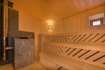 Sauna with benches made of light wood in a traditional style. The heating element 
is decorated with gray marble tiles.