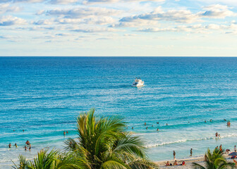 People enjoying the beach and swimming in the clear blue waters of Cancun Hotel Zone with a boat cruising offshore under a partly cloudy sky High-quality photo.