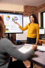 Businesswoman discussing project updates with colleague and reviewing company status on digital...