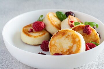 Fresh cottage cheese or ricotta  pancakes (syrniki,fritters) on a white plate with fresh berries on a blue background. Delicious healthy breakfast.  Ukrainian, Russian cuisine sweet food.