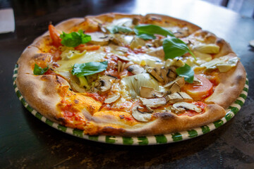 Delicious vegetarian pizza topped with fresh vegetables and herbs served on a decorative plate in a...