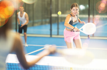 Young girl paired with a man plays padel on an indoor tennis court
