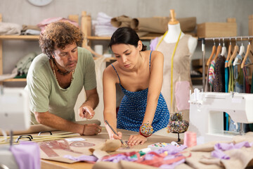 Woman and man tailor draw dress pattern with curve ruler on paper and participate in creating...