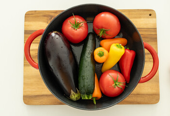 red beautiful cast iron skillet and fresh vegetables. cooking vegetable stew in cast iron. fresh...
