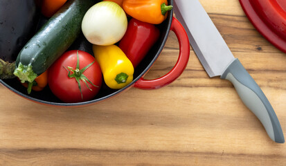 top view cutting board with knife and fresh vegetables: carrots, eggplant, tomatoes, onions,...