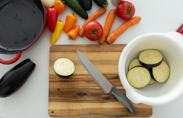 top view cutting board with knife and fresh vegetables: carrots, eggplant, tomatoes, onions,...