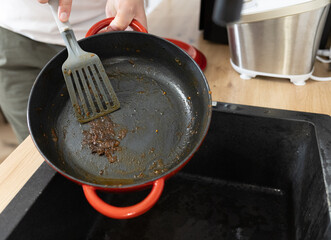 man in kitchen trying to clean food burnt to cast iron pan, hand washing cast iron cookware