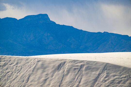 Thick white sand dunes with mountains and rain falling in the background at White Sands National Park, New Mexico