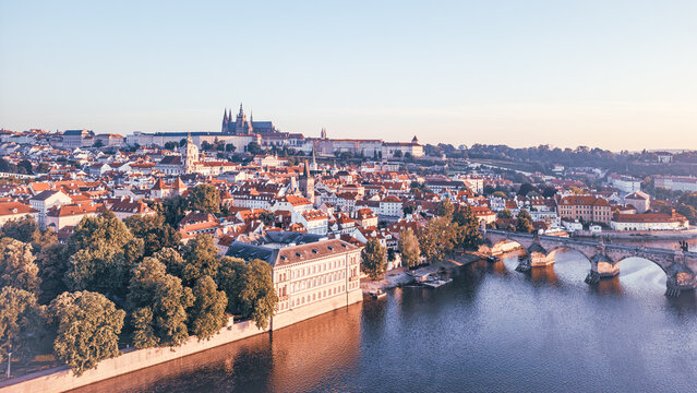 Morning light casts a warm glow on Prague's medieval cityscape, revealing the iconic Charles Bridge and Hradcany Castle along the Vltava River. A breathtaking aerial view captivates. - Powered by Adobe