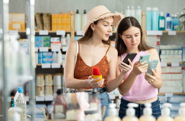 Near display case in pharmacy, mom and daughter scans barcode on sunblock cream, reads user manual....
