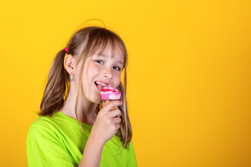 Happy little blonde girl eating ice cream against yellow background. Studio shot