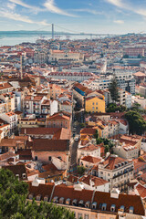 Fototapeta premium Vibrant aerial view of Lisbon, Portugal, featuring traditional red rooftops, winding streets, and the famous 25 de Abril Bridge under a bright blue sky, perfect for travel blogs.