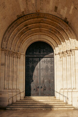 Obraz premium Beautiful Romanesque church entrance in Lisbon, Portugal, featuring intricate stone arches and a grand wooden door, ideal for architecture, travel, and heritage concepts.