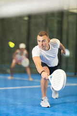 Male players playing padel in a padel court indoor behind the net