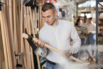 Young man shopper choosing hoe in gardening department of hardware store