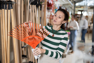 Woman chooses and buys rake at a hardware store for gardening.