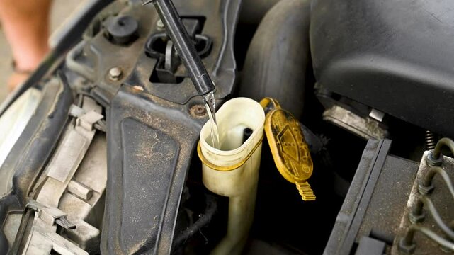 Man filling water into windscreen water tank in car engine room, for window wiper 