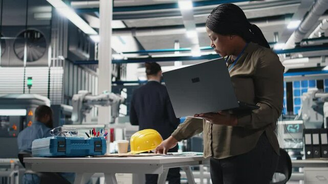 Woman master engineer examining production line for photovoltaics, reviewing manufacturing process data on laptop. Working on alternative energy success for industrial operations. Camera B.