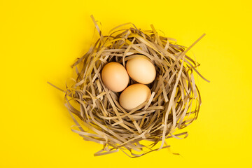 Three eggs in straw nest – top view,yellow background