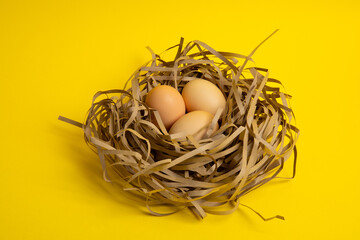Three brown eggs in paper nest – yellow background, top view