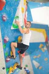 Sporty man grabbing ledges of artificial climbing wall in bouldering centre