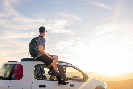 Traveler enjoying the sunset from the car roof during a road trip. Peaceful moment of reflection, adventure, and freedom on the open road.