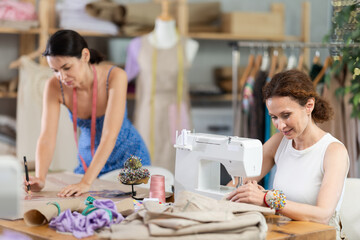 Woman tailor draw dress pattern with curve ruler on paper, female master seamstress sewing cloth with sewing machine. Tailor workplace with cut textile, sewing machine, thread, pins, needles, tape