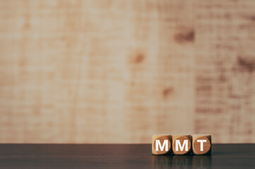 There is wood cube with the word MMT. It is an abbreviation for Modern Monetary Theory as...
