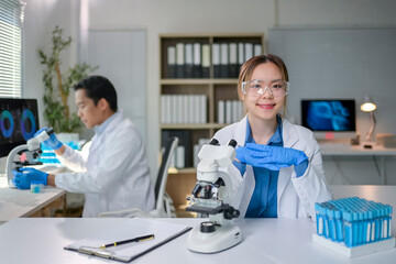 Fototapeta premium Young scientist smiling at camera with microscope and test tubes in laboratory