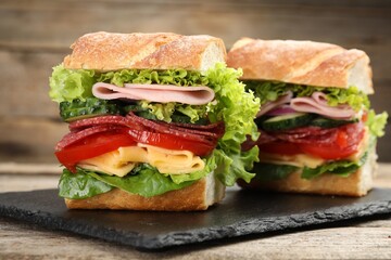 Tasty baguette sandwich with ham and vegetables on wooden table, closeup
