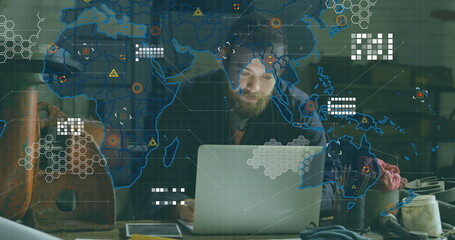 Hoodie-clad man analyzing laptop data map overlay at workbench, with power drill and measuring tape