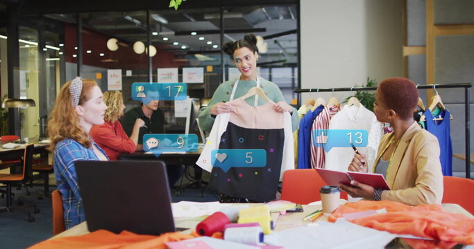 Presenting designer holding two-tone dress on hanger in open-plan workspace, with social icons