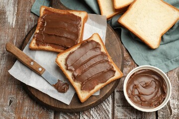 Sandwiches with chocolate butter and knife on wooden table, flat lay